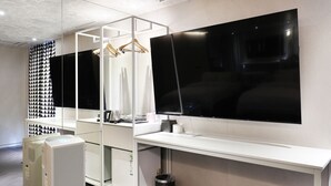 A modern room with a large flat-screen TV mounted on the wall, a white desk, and a hanging clothes rack. - Hotel The Designers Jongno (Seoul)