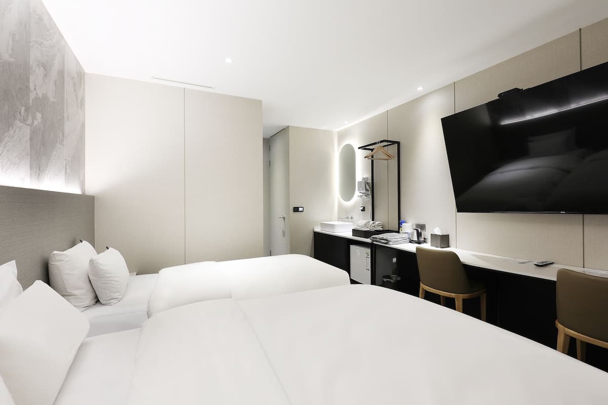 Una habitación de hotel moderna con una cama grande, un escritorio con televisor de pantalla plana, un espejo y una pequeña cocina.