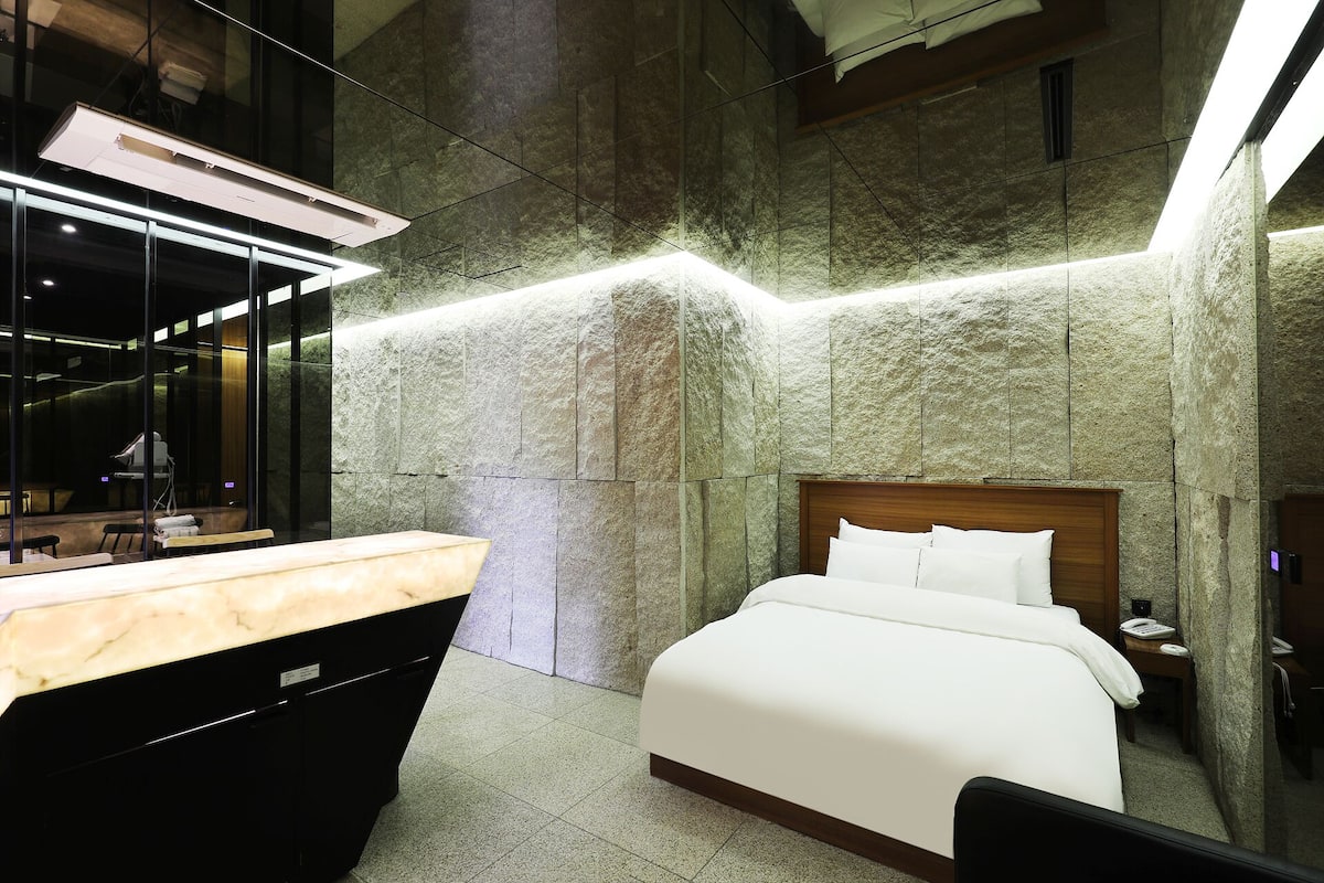 Una habitación de hotel moderna con una cama grande, cabecera de madera, una mesita de noche y un espejo amplio.