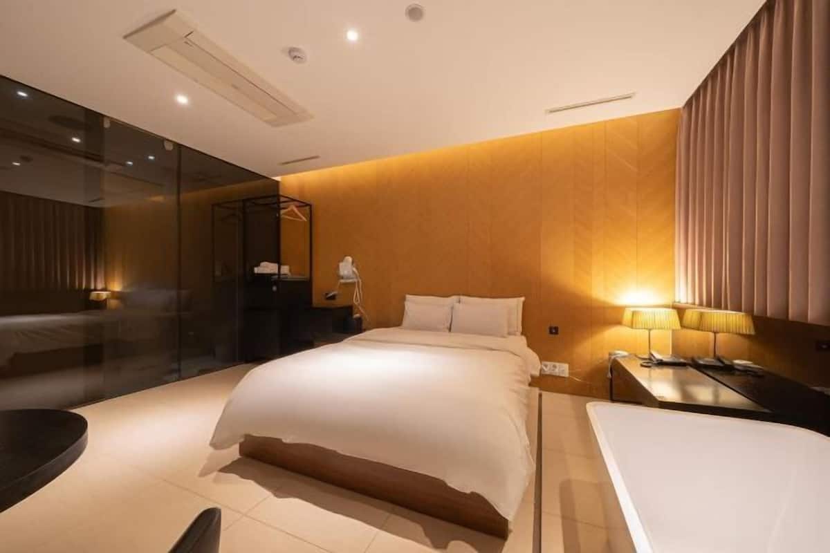 Una habitación de hotel moderna con una cama grande, mesitas de noche, un espejo y un separador de vidrio.