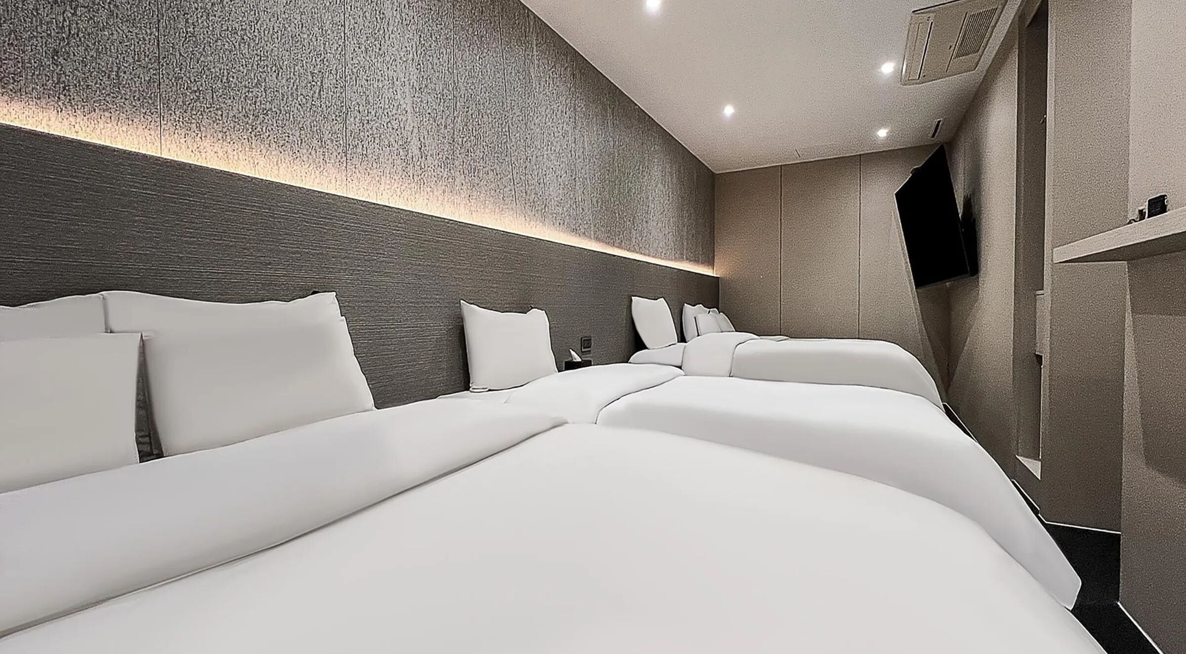 A hotel room with a modern design, featuring a large bed with white linens, a textured wall, and a built-in wardrobe.