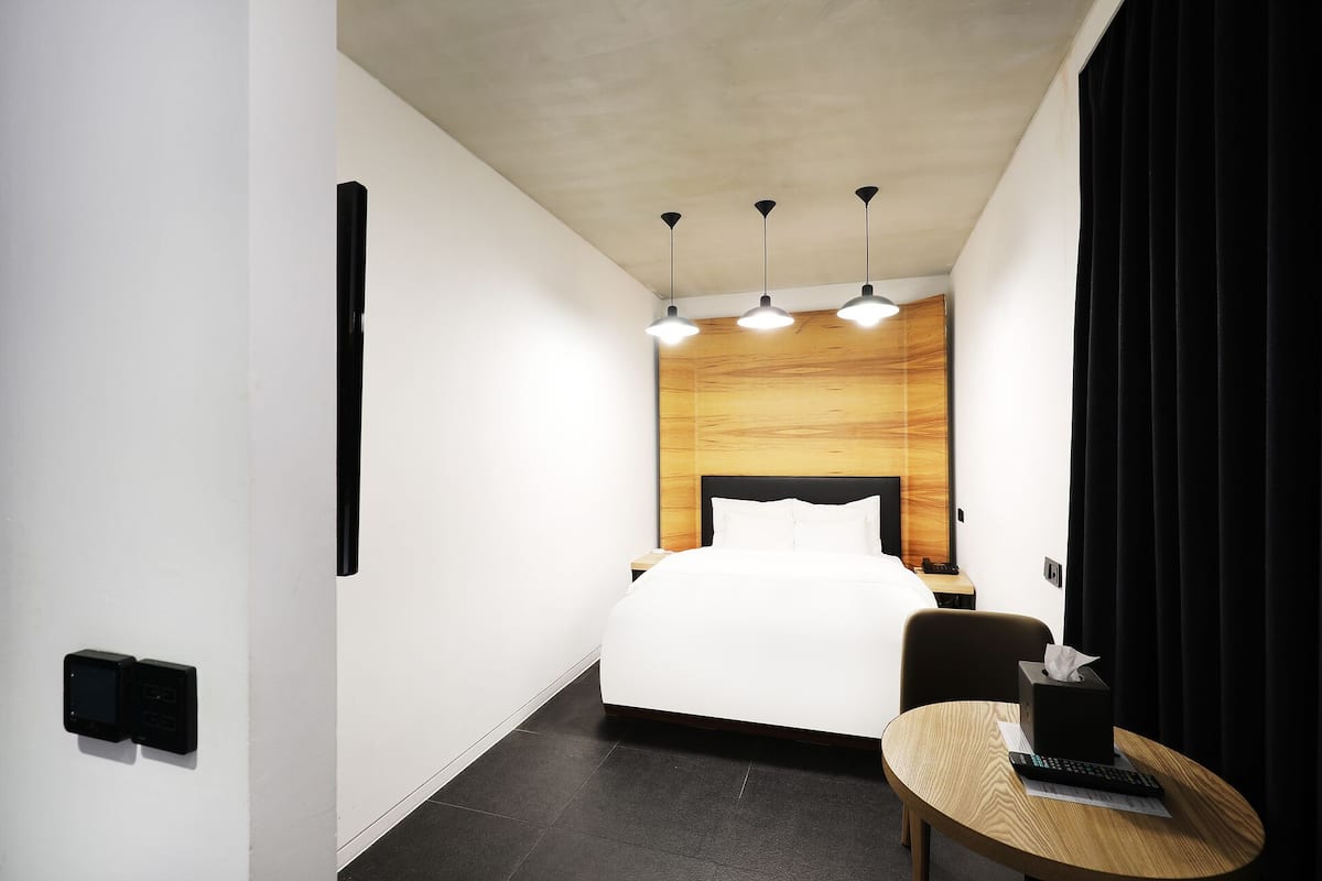 Habitación de hotel con cama, mesita de noche y una pequeña mesa redonda con un control remoto y pañuelos.