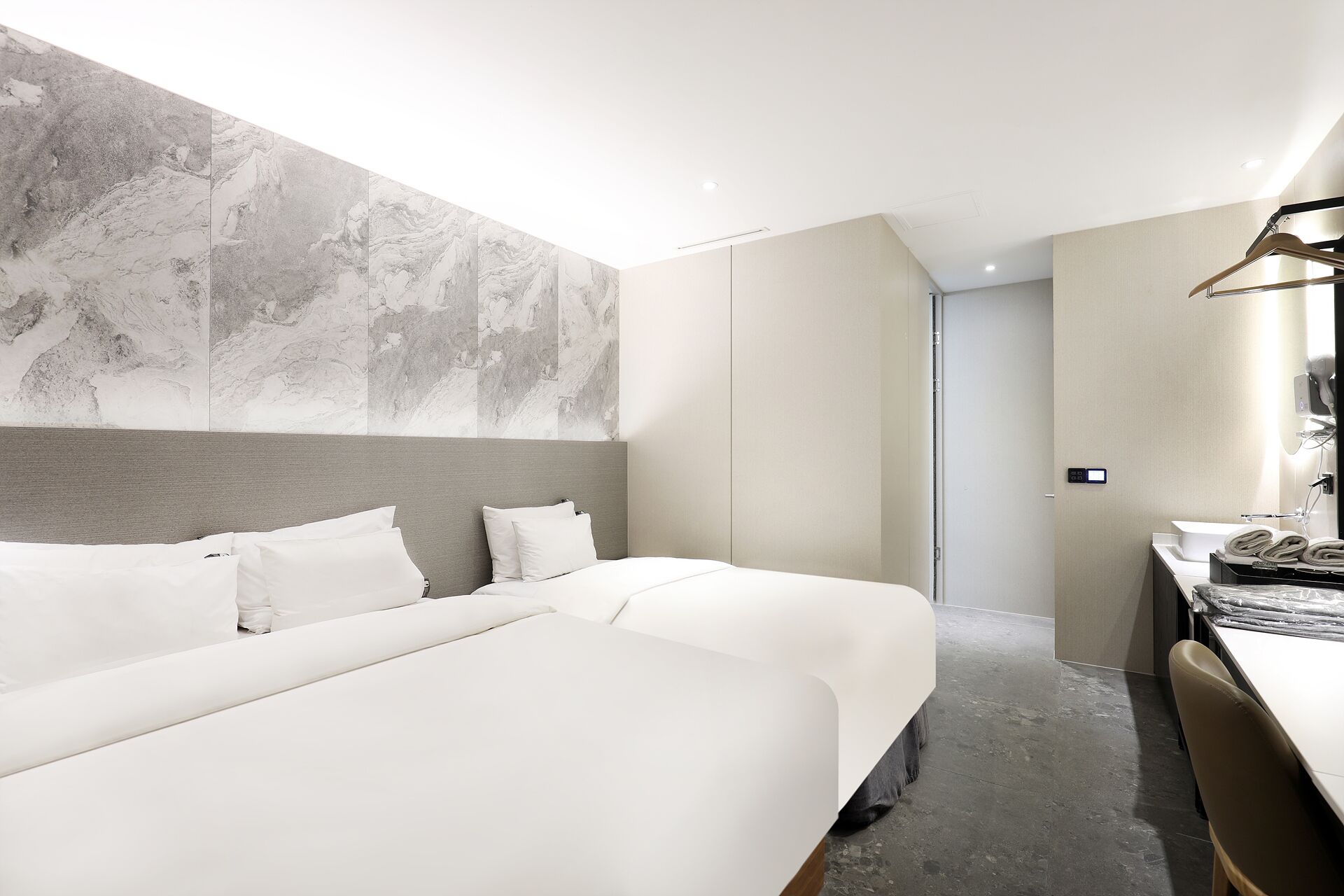 A hotel room with two beds, a desk, and a bathroom.