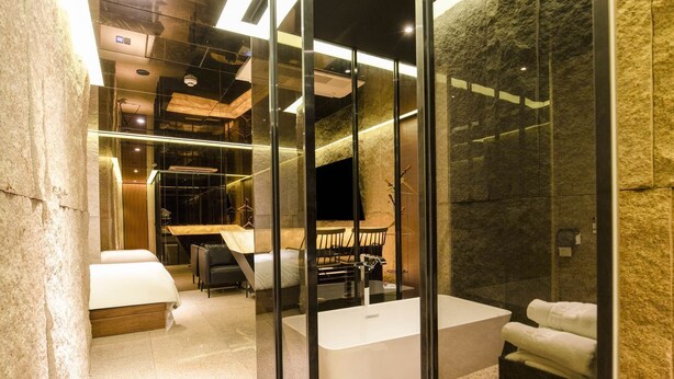 A modern hotel room with a glass partition, a large bed, a desk, and a bathroom with a bathtub. - Hotel The Designers Jongno (Seoul)
