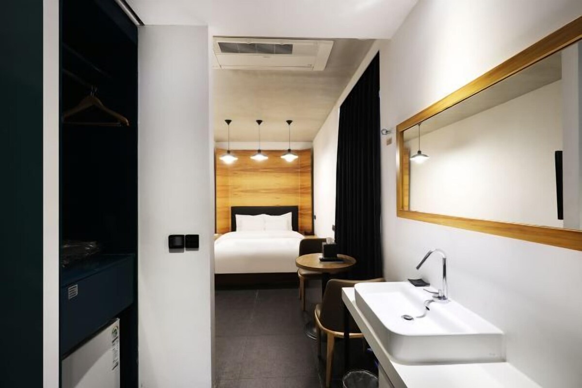 Habitación de hotel con cama, mesita de noche, espejo, lavamanos y una pequeña mesa redonda.