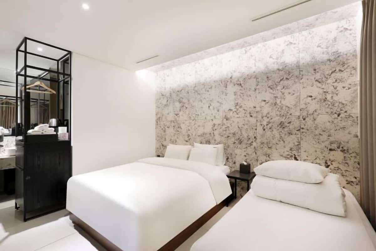 Habitación de hotel con dos camas, un espacio para vestirse con espejo y una pared con diseño de mármol.