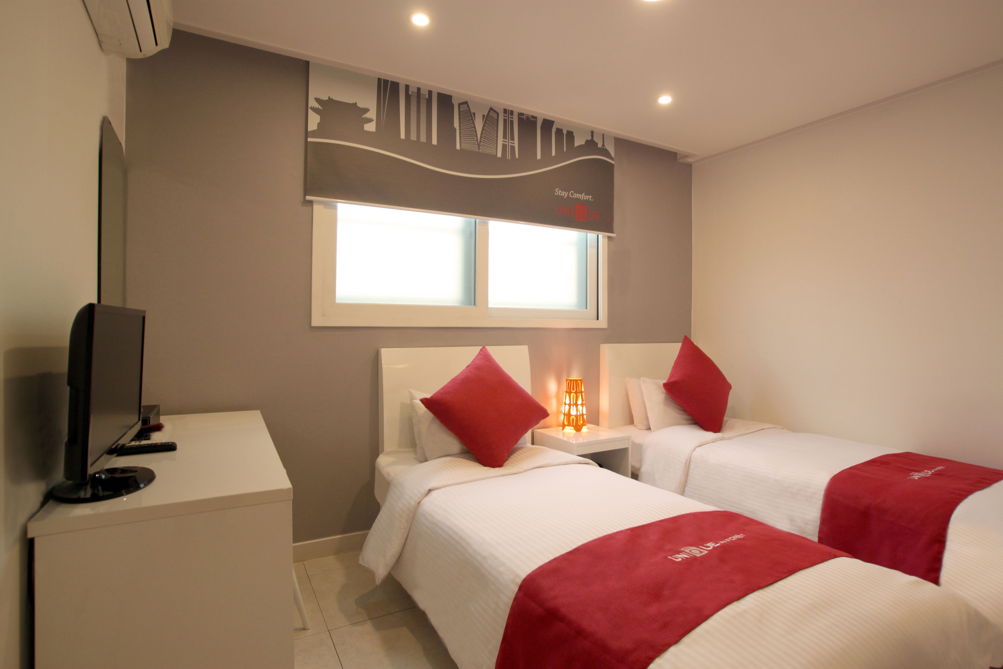 Habitación de hotel con dos camas, televisión, mesita de noche y ventana con persianas.