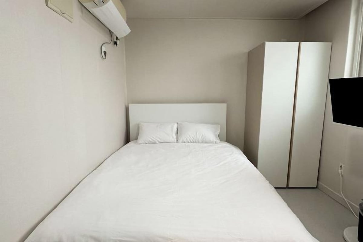 A minimalist hotel room with a single bed, a wardrobe, and a television.