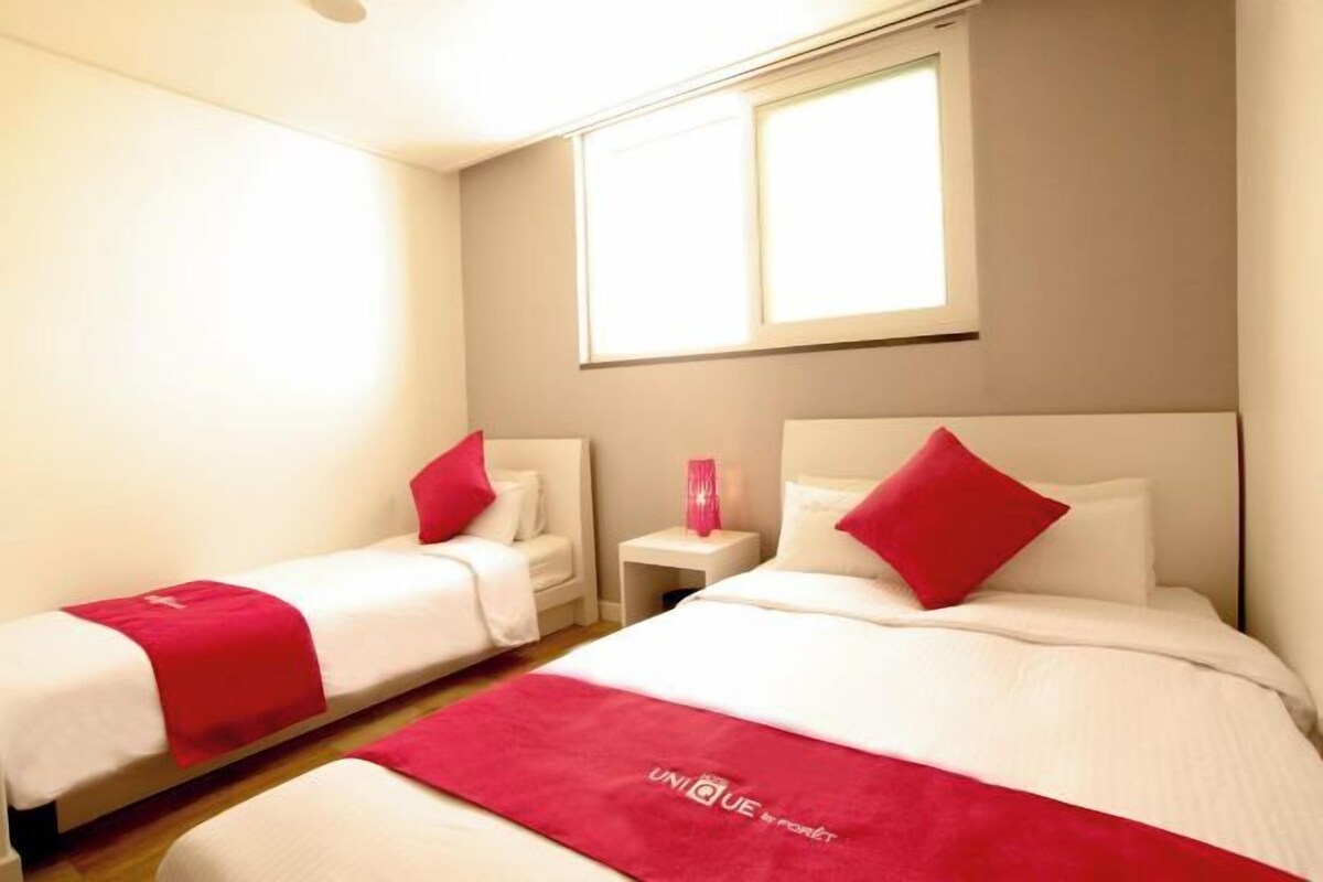 A hotel room with two beds, a window, and a nightstand with a vase.