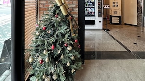 Ein Weihnachtsbaum mit Dekorationen und einem Geschenk an einer Ziegelwand mit Fenster und Verkaufsautomat.