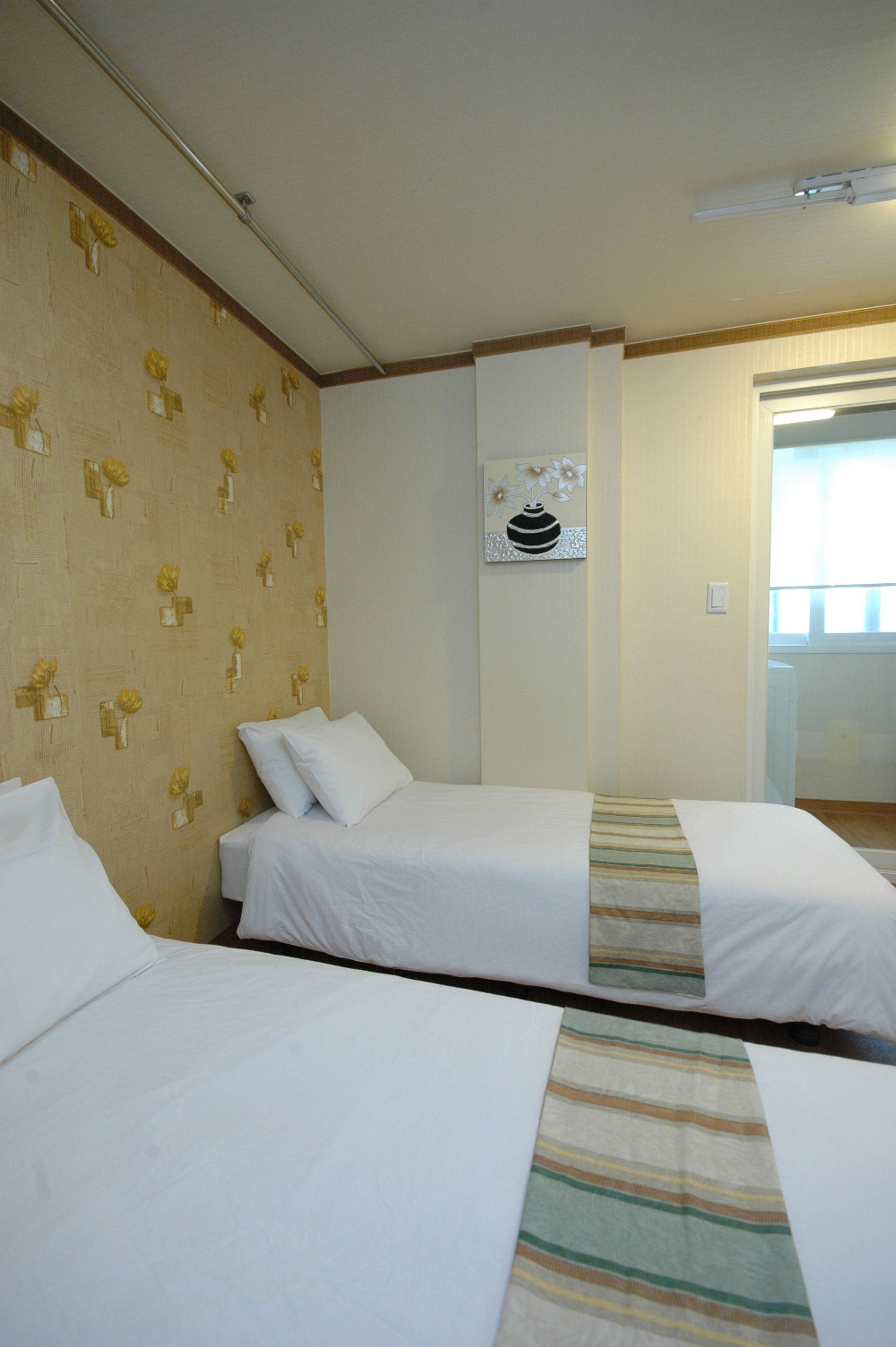 A hotel room with two beds, a wall-mounted air conditioning unit, and a door leading to a bathroom.