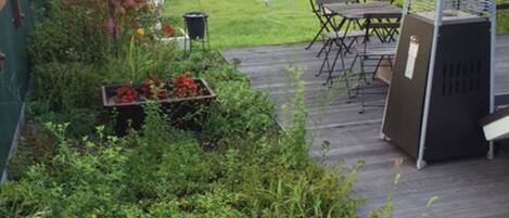 A rooftop garden with a wooden deck, a grill, and a seating area.