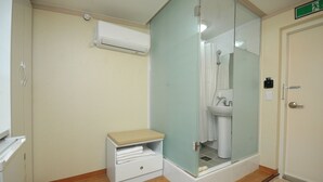 Een badkamer met een douchecabine van glas, een witte wastafel en een klein bankje met handdoeken.