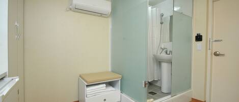 A bathroom with a glass shower enclosure, a white sink, and a small bench with towels.