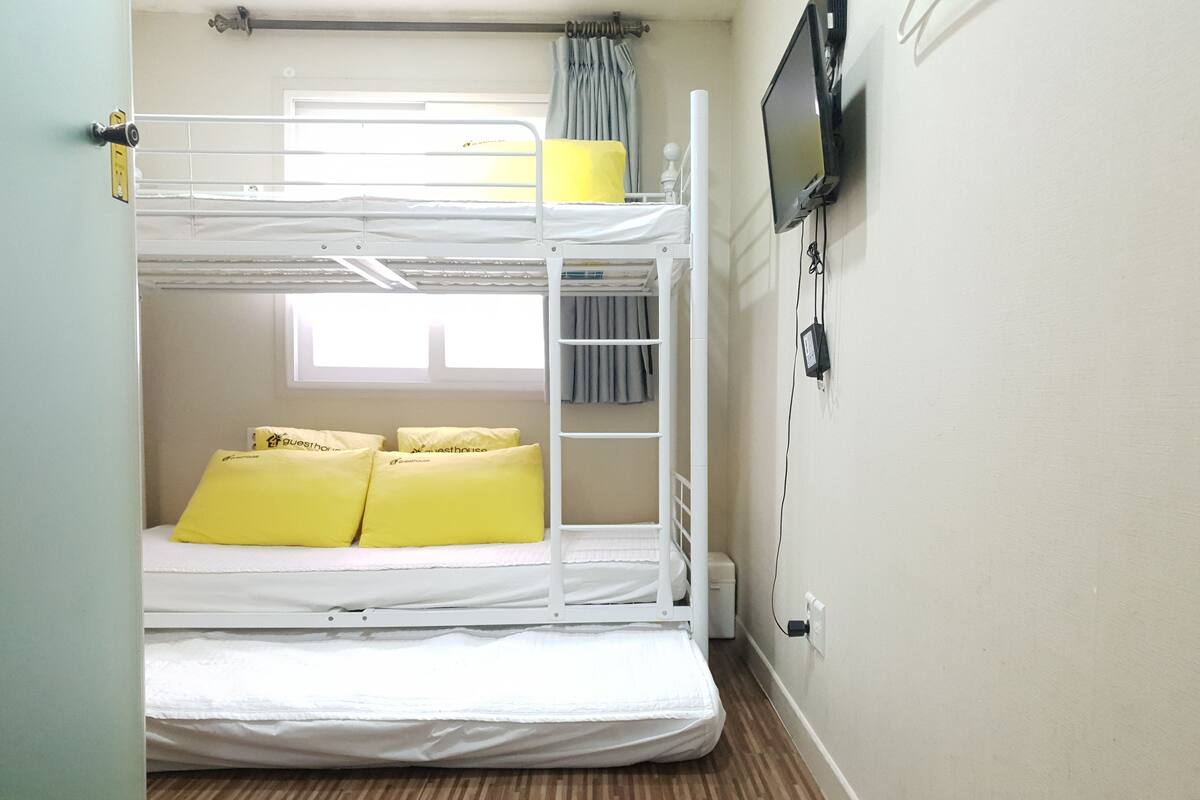 Habitación con literas, televisor en la pared, ventana con cortinas y piso de madera.