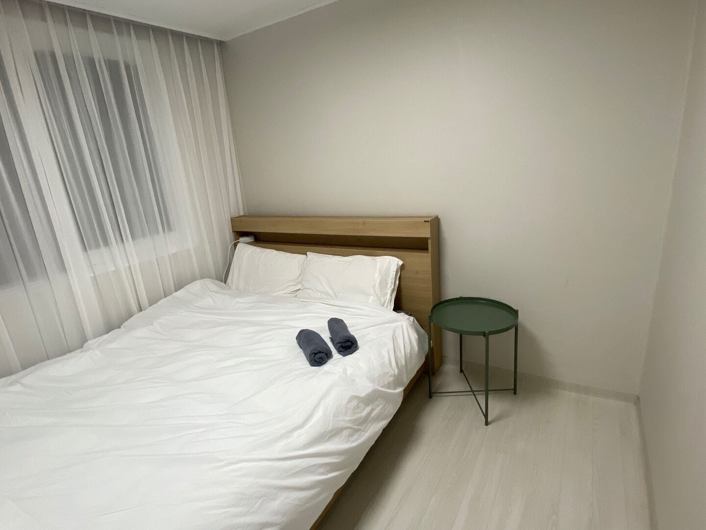 A neatly made bed with white linens and a pair of rolled-up gray pants on the footboard.