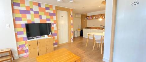 A modern living room with a wooden coffee table, a TV on a wooden cabinet, and a colorful wall.