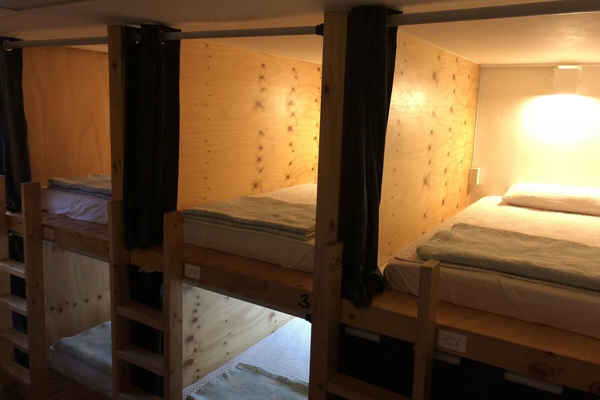 A dormitory-style room with bunk beds, wooden walls, and a single light source.