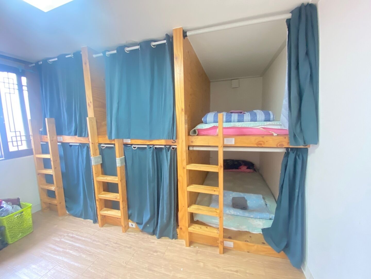 Habitación con literas, una escalera, una ventana con cortinas y una pequeña cesta verde en el suelo.