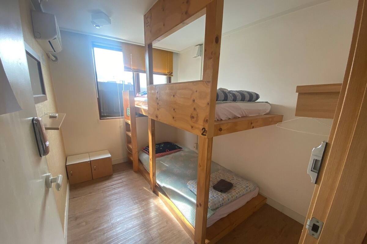 A compact room with a bunk bed, a small desk, and a window.