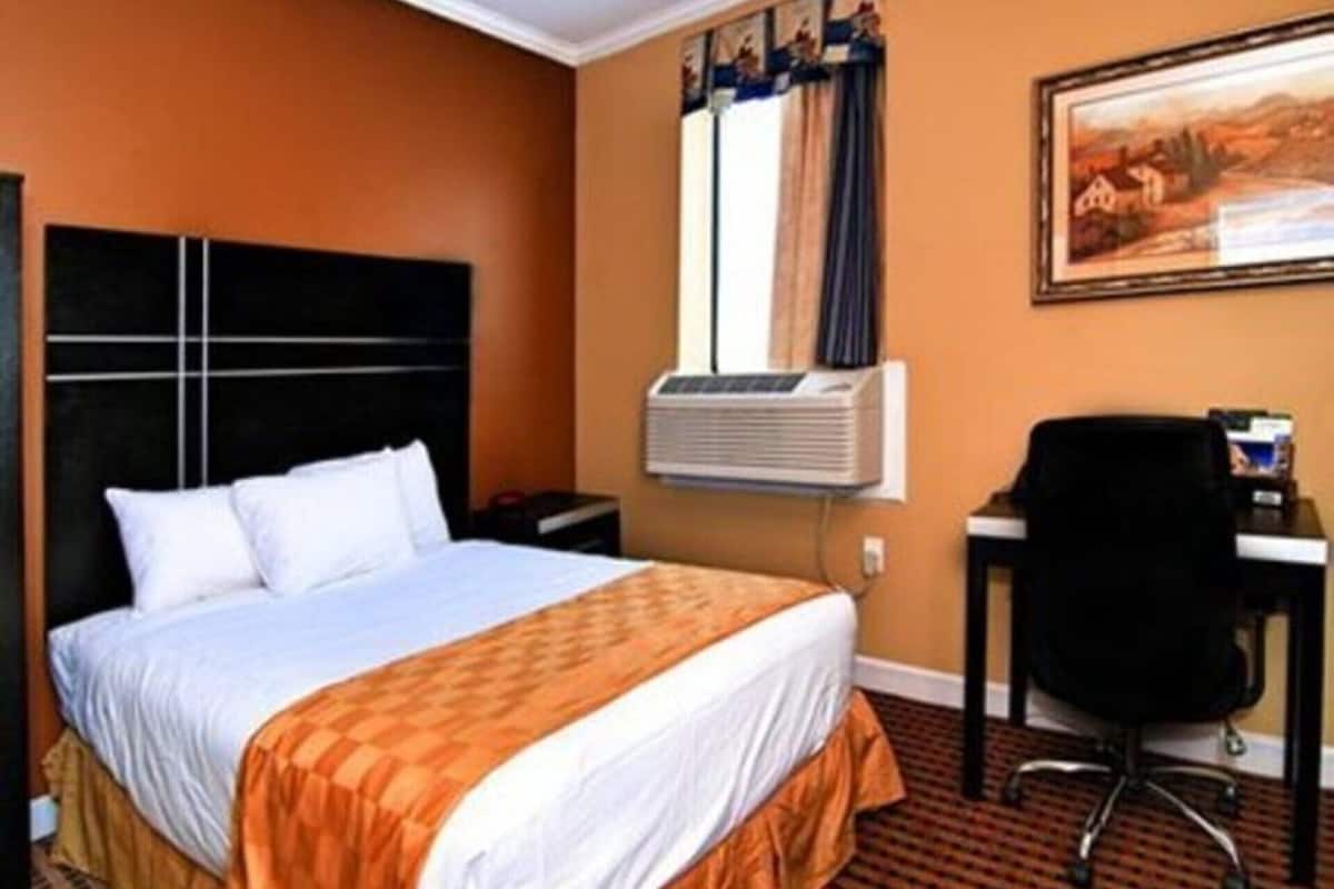 A hotel room with a bed, an air conditioning unit, a desk, and a chair.