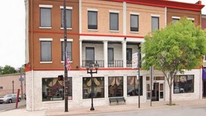A two-story building with a red roof and a white facade. There is a bench outside and a tree in front.