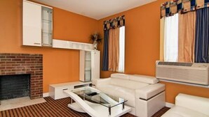 A living room with a brick fireplace, white sofa, glass coffee table, and a large window with curtains.