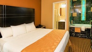 A hotel room with a large bed, a headboard, a bathroom with a mirror and sink, and a patterned carpet.