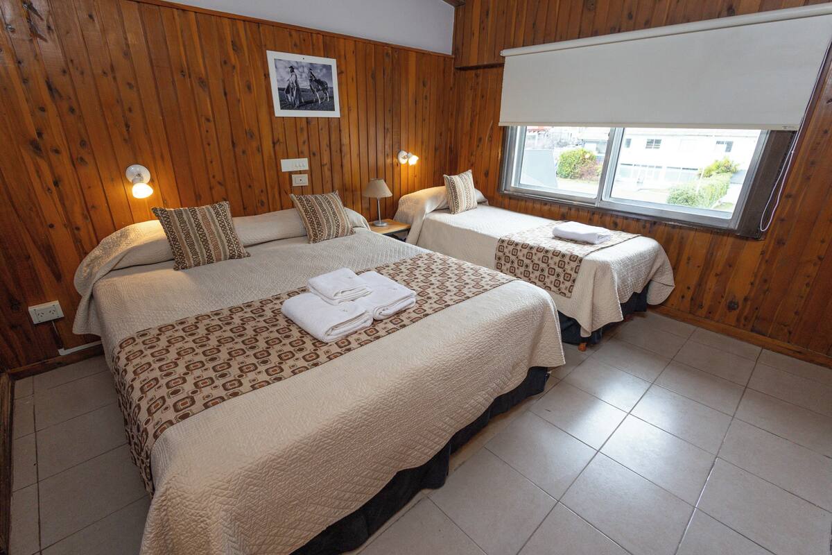 Habitación de hotel con dos camas, paredes de paneles de madera, ventana con vistas e imagen enmarcada en la pared.