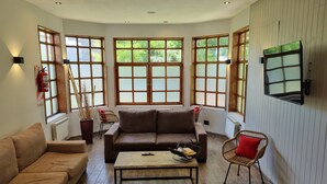 A spacious living room with a brown sofa, a coffee table, and wicker chairs. Large windows allow natural light and views of greenery. - Tierra Gaucha Hotel Boutique (San Carlos de Bariloche)
