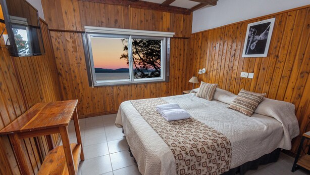A wooden-paneled room with a bed, a bench, and a window with a view. - Tierra Gaucha Hotel Boutique (San Carlos de Bariloche)