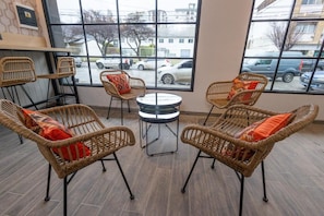 Un coin salon avec des fauteuils en osier et une petite table ronde, de grandes fenêtres offrant une vue sur les voitures et les bâtiments qui se trouvent à l’extérieur.