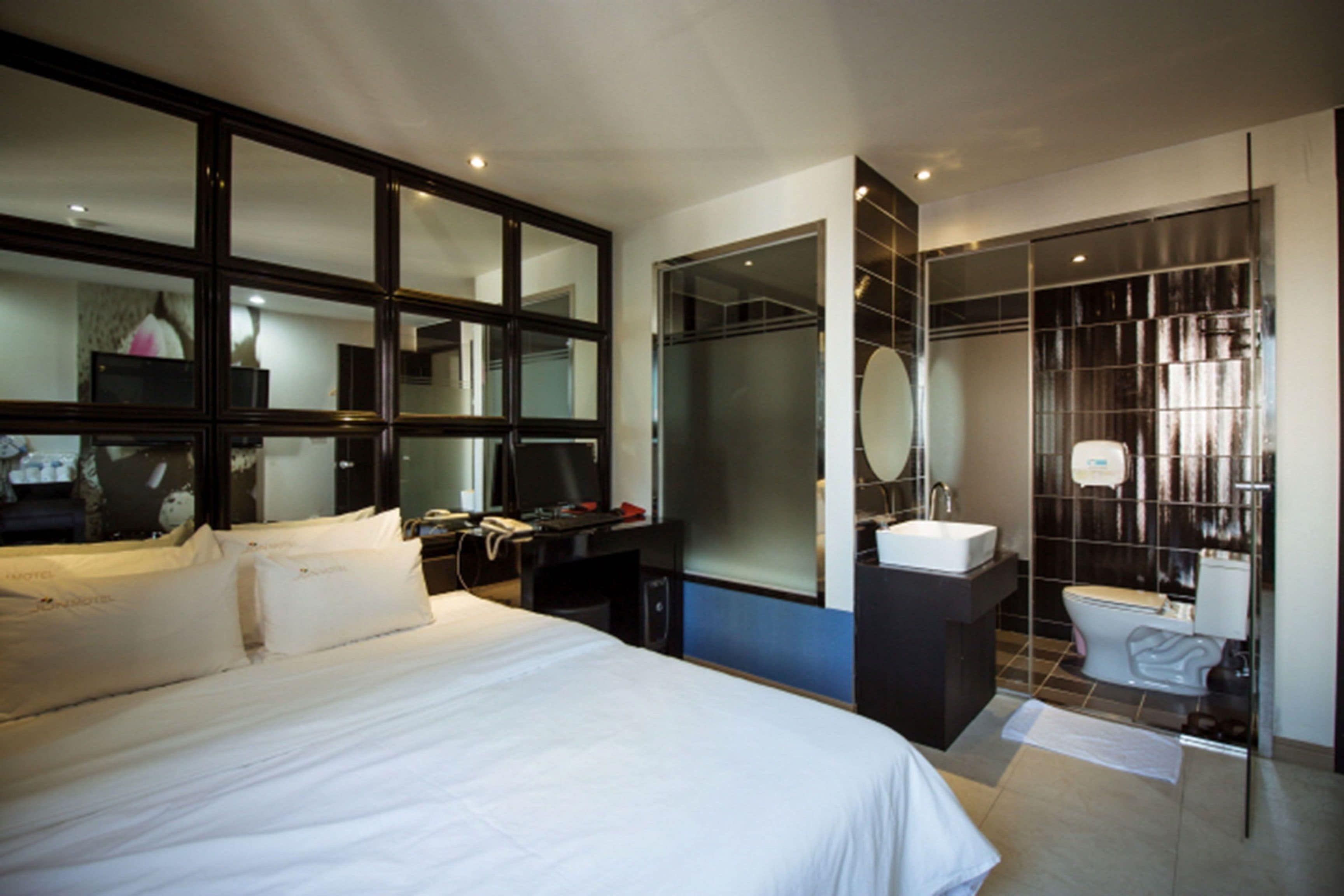Quarto de hotel moderno com uma cama grande, uma escrivaninha, um espelho e um banheiro com vaso sanitário e área de chuveiro.