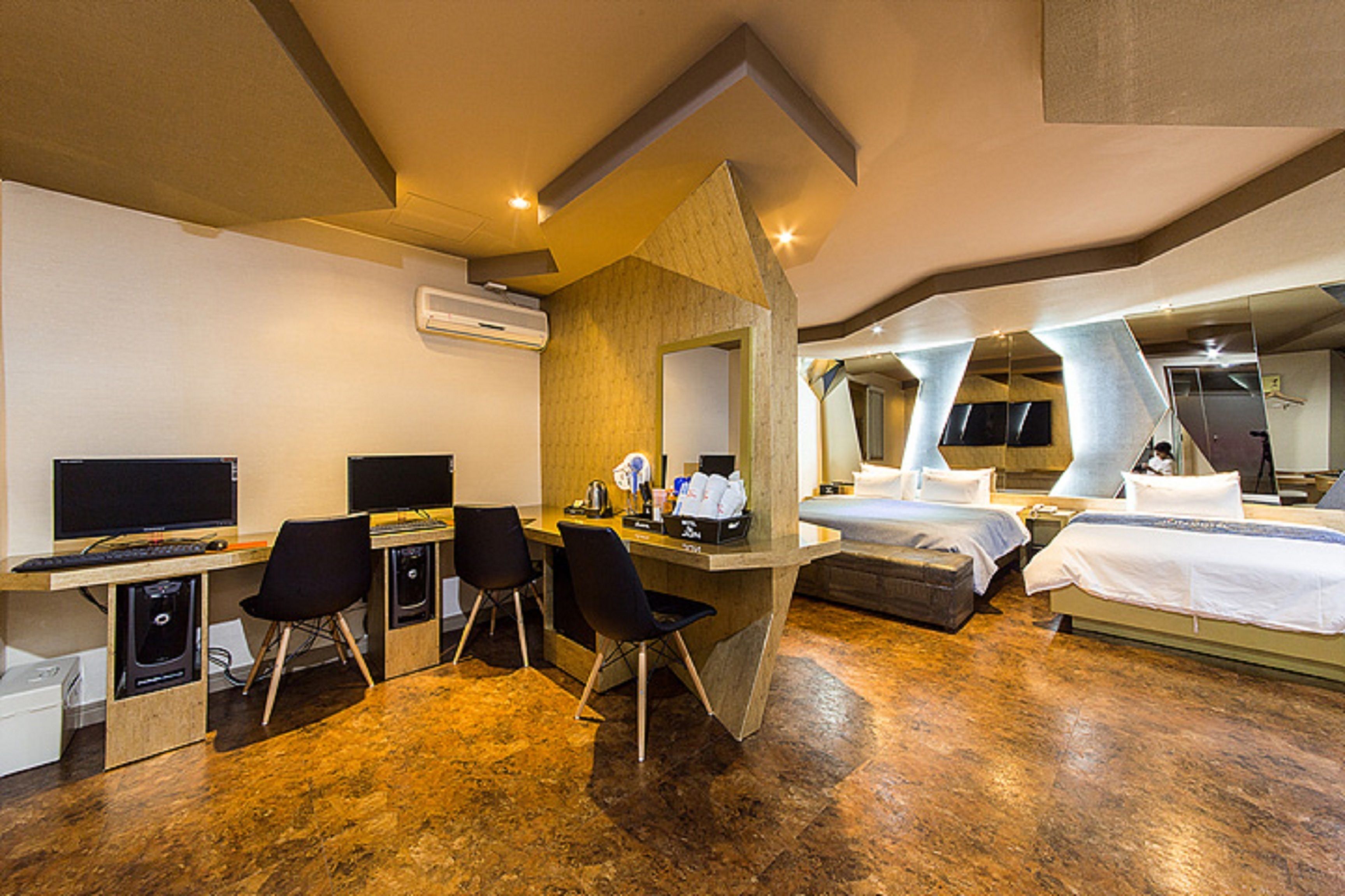 Quarto de hotel com escrivaninha, duas cadeiras, uma cama e uma televisão.