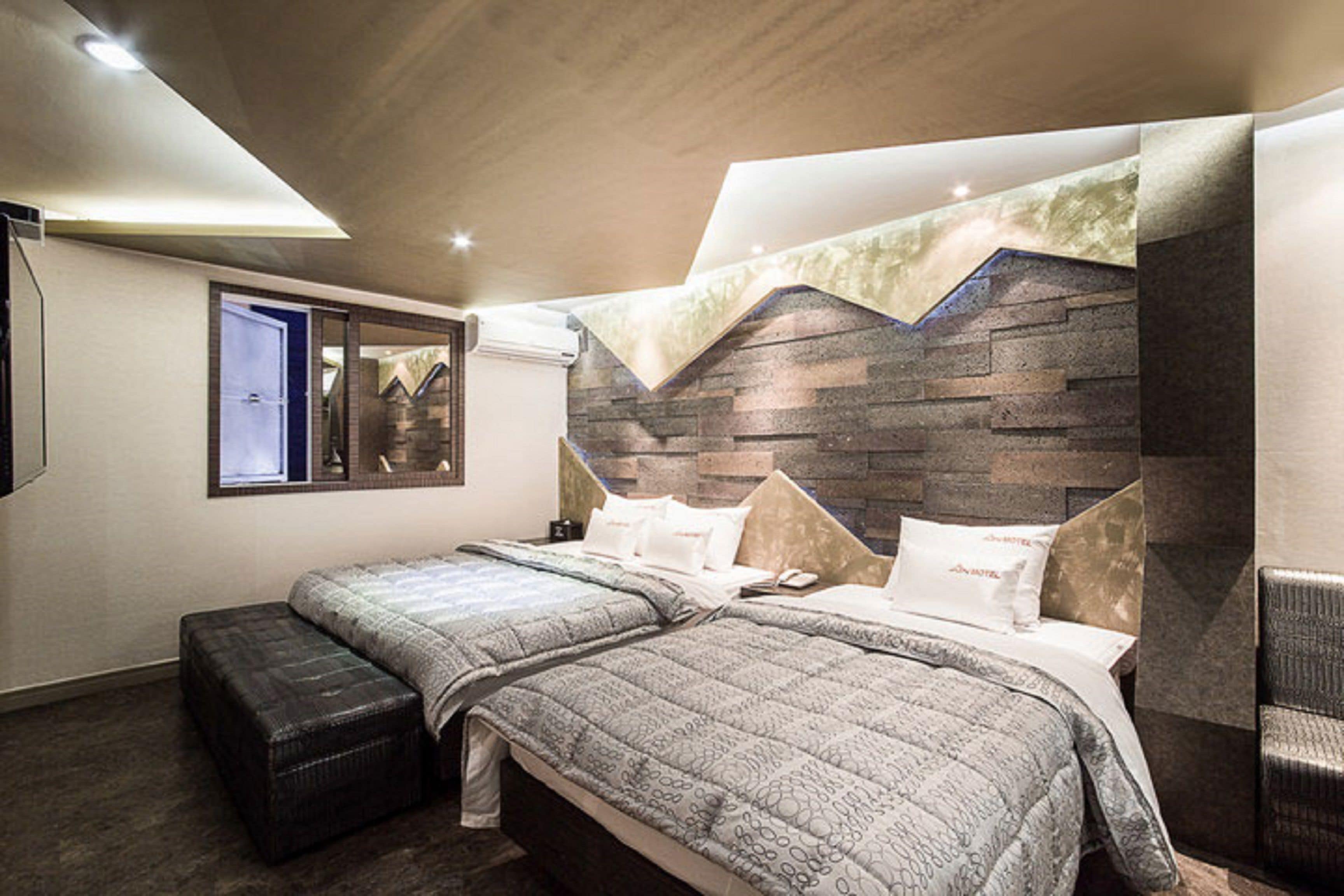 Un dormitorio moderno con dos camas, un ventanal grande y un cabecero con estampado de piedra.