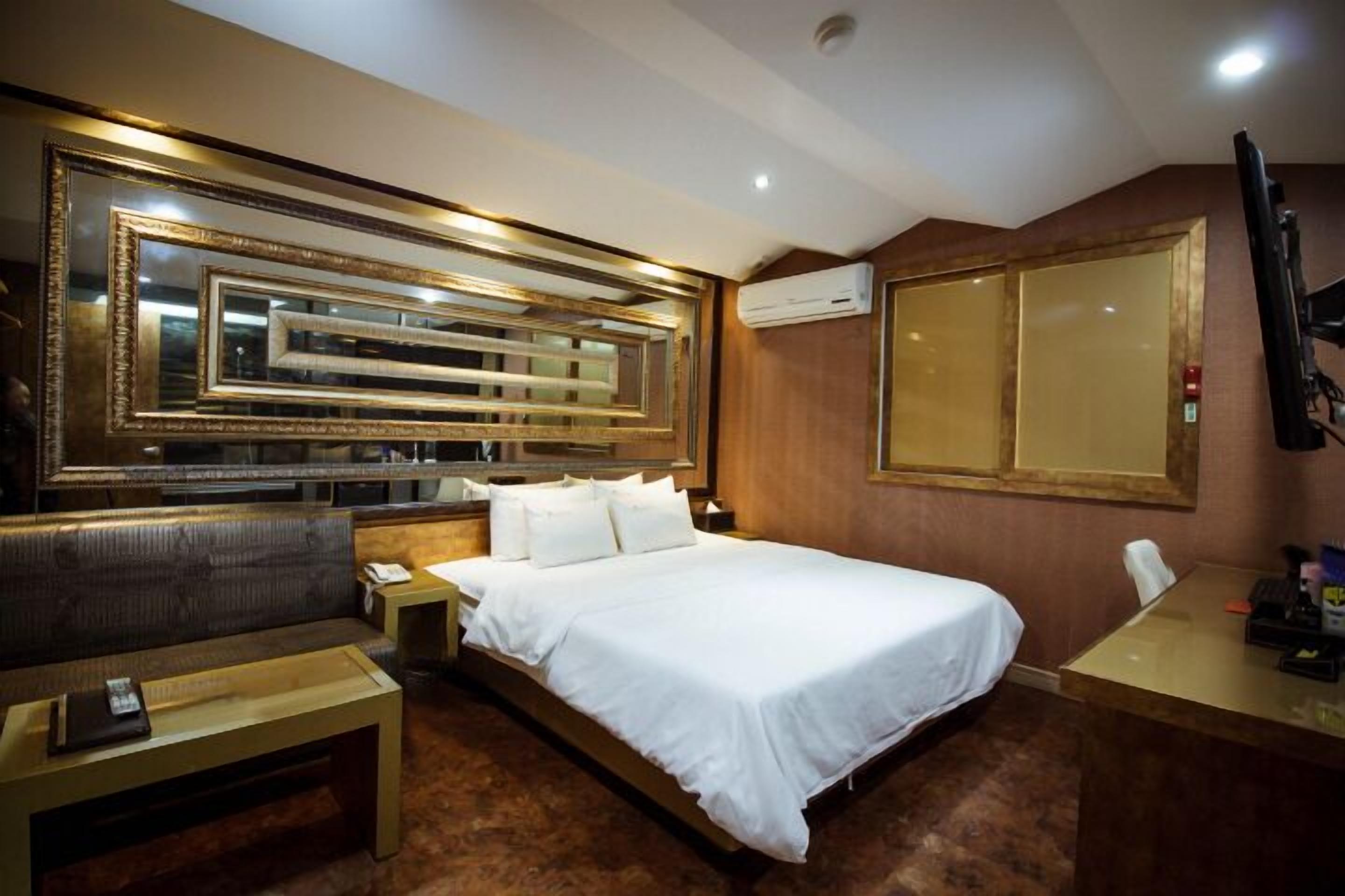 A hotel room with a large bed, a sofa, a desk, and a mirror.