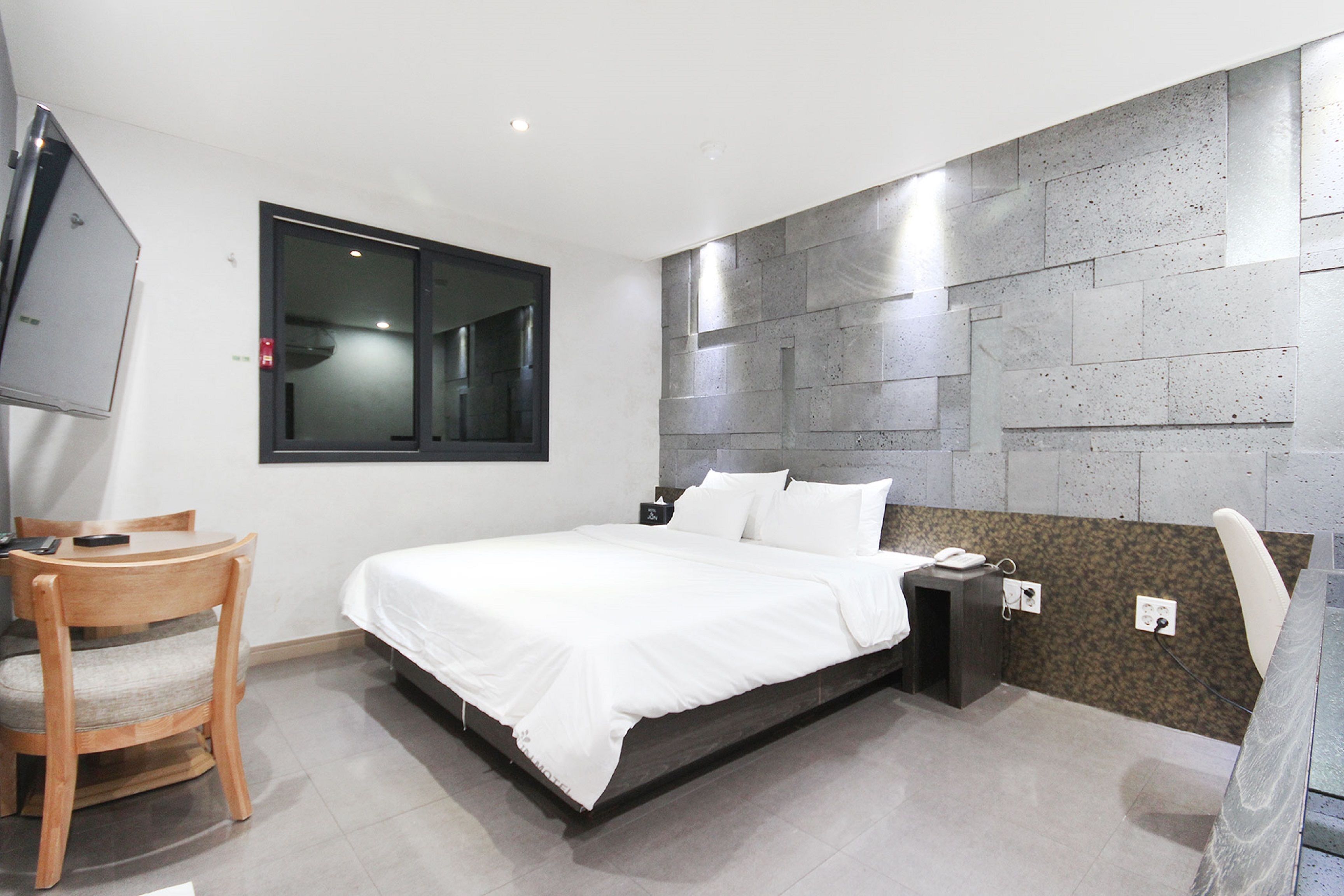 A modern bedroom with a bed, bedside table, chair, and a TV mounted on the wall.