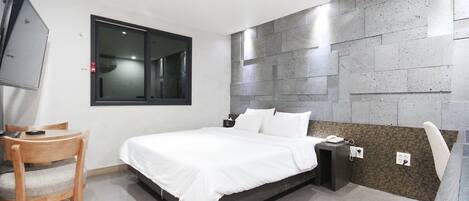 A modern bedroom with a bed, bedside table, chair, and a TV mounted on the wall.