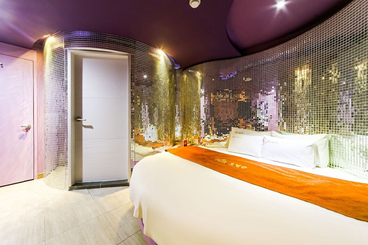 A modern hotel room with a large bed, a door with a number, and a wall with a mosaic design.