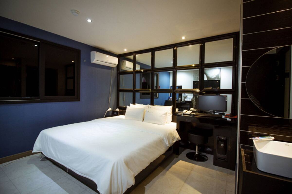 A modern hotel room with a large bed, a desk with a computer, and a bathroom.