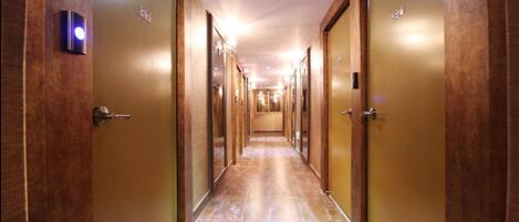 A long, narrow hotel corridor with wooden doors on both sides and a tiled floor.