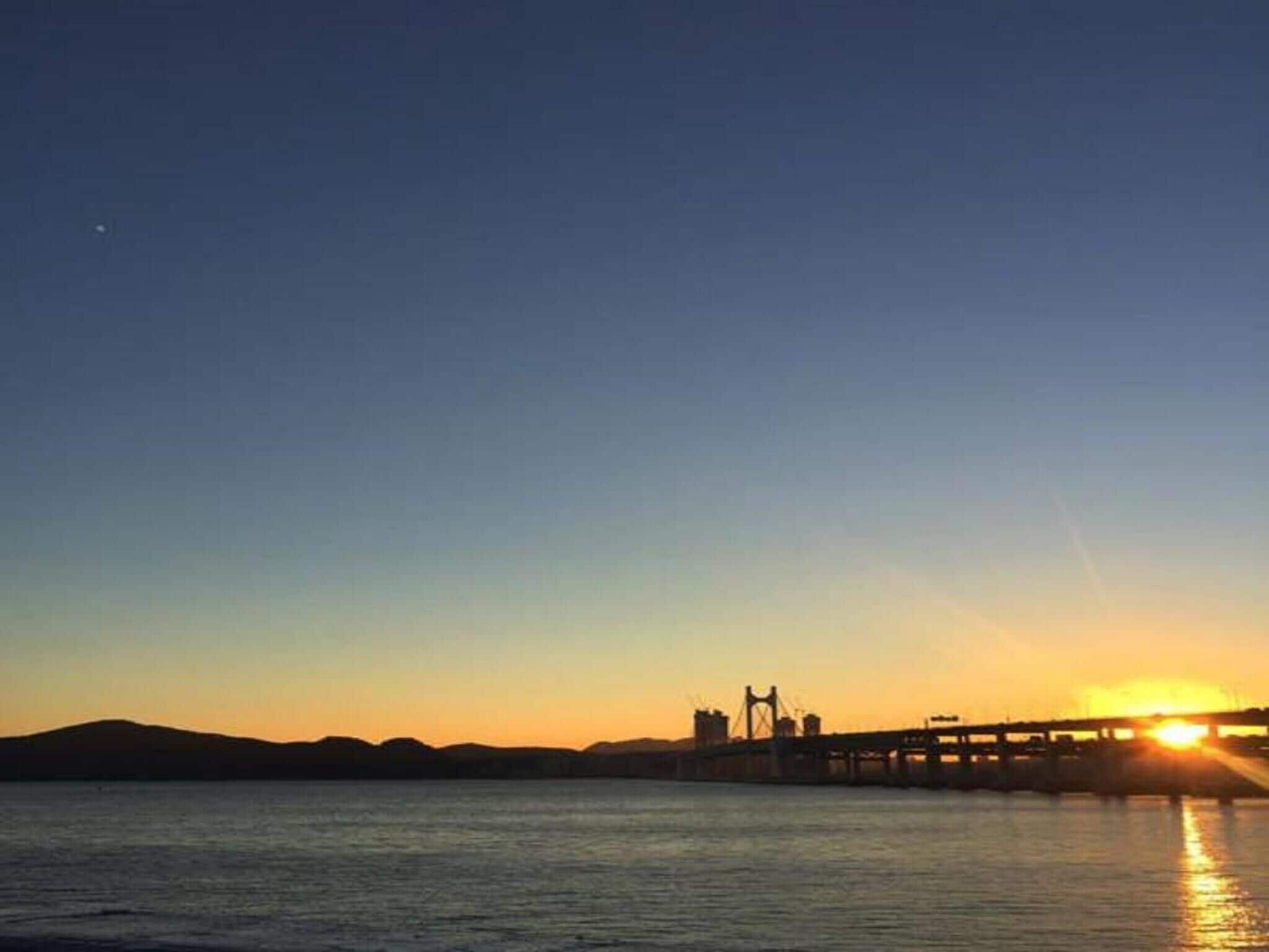 Un atardecer sobre un cuerpo de agua con un puente y colinas a lo lejos.