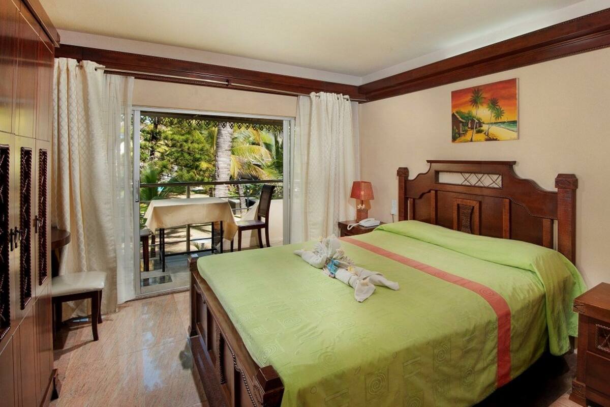 A hotel room with a bed, a desk, a chair, a nightstand, and a painting on the wall.