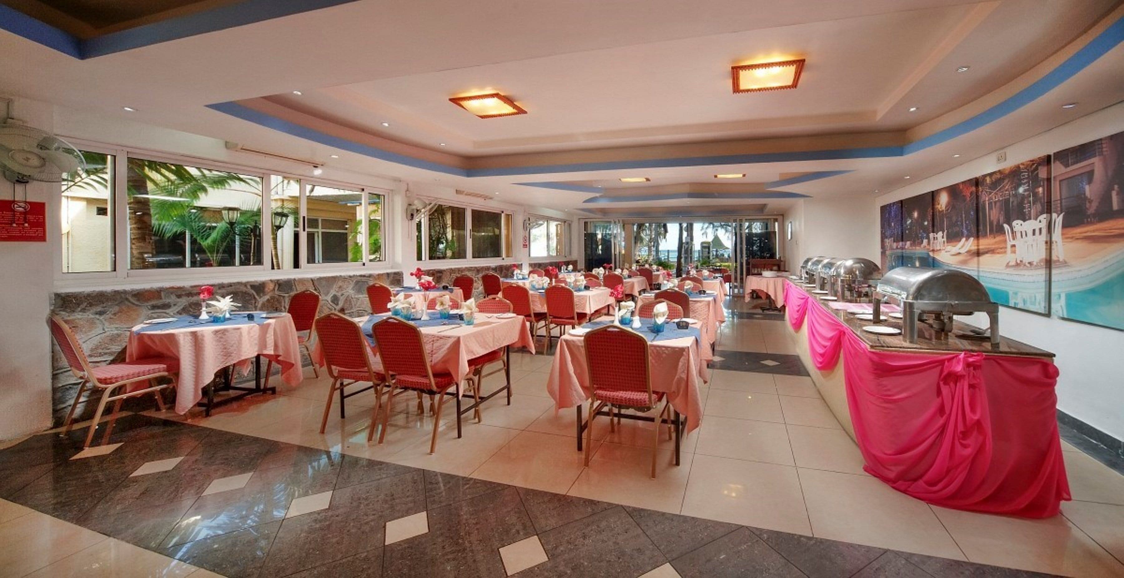 A spacious dining area with multiple tables and chairs, large windows, and a view of the outdoors.