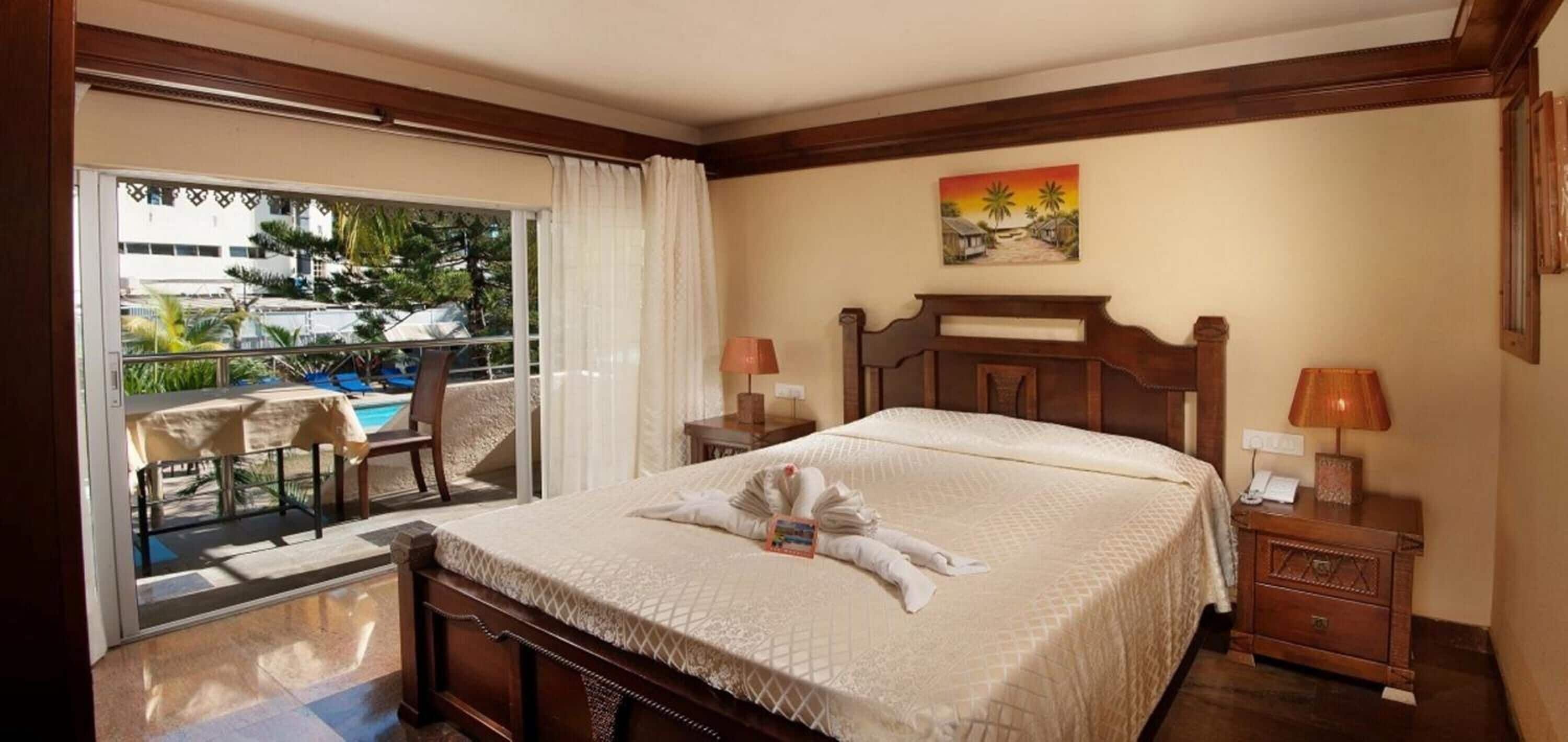 Une chambre d’hôtel comprenant un lit, une table de chevet, une chaise, une table et une vue sur une piscine et la verdure environnante.
