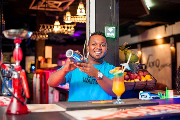 Zona de bar con un cantinero, una cesta de fruta y un cartel de Wi-Fi.