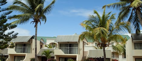 A resort with multiple two-story buildings, palm trees, and a small outdoor seating area.