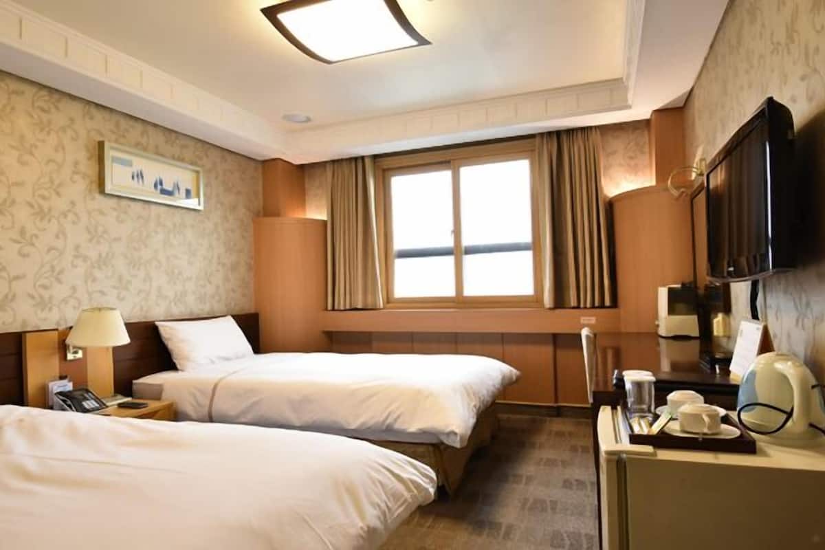 Habitación de hotel con dos camas, un televisor, un escritorio con teléfono y una ventana con cortinas.