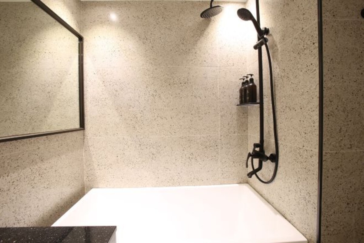 Une salle de bain moderne avec un lavabo blanc, une douche équipée d’un pommeau de douche à main et un miroir au mur.