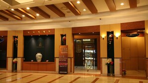 A hotel lobby with a reception desk, a business room sign, and a display case with a vase. - Hotel Samwon Plaza (Anyang)